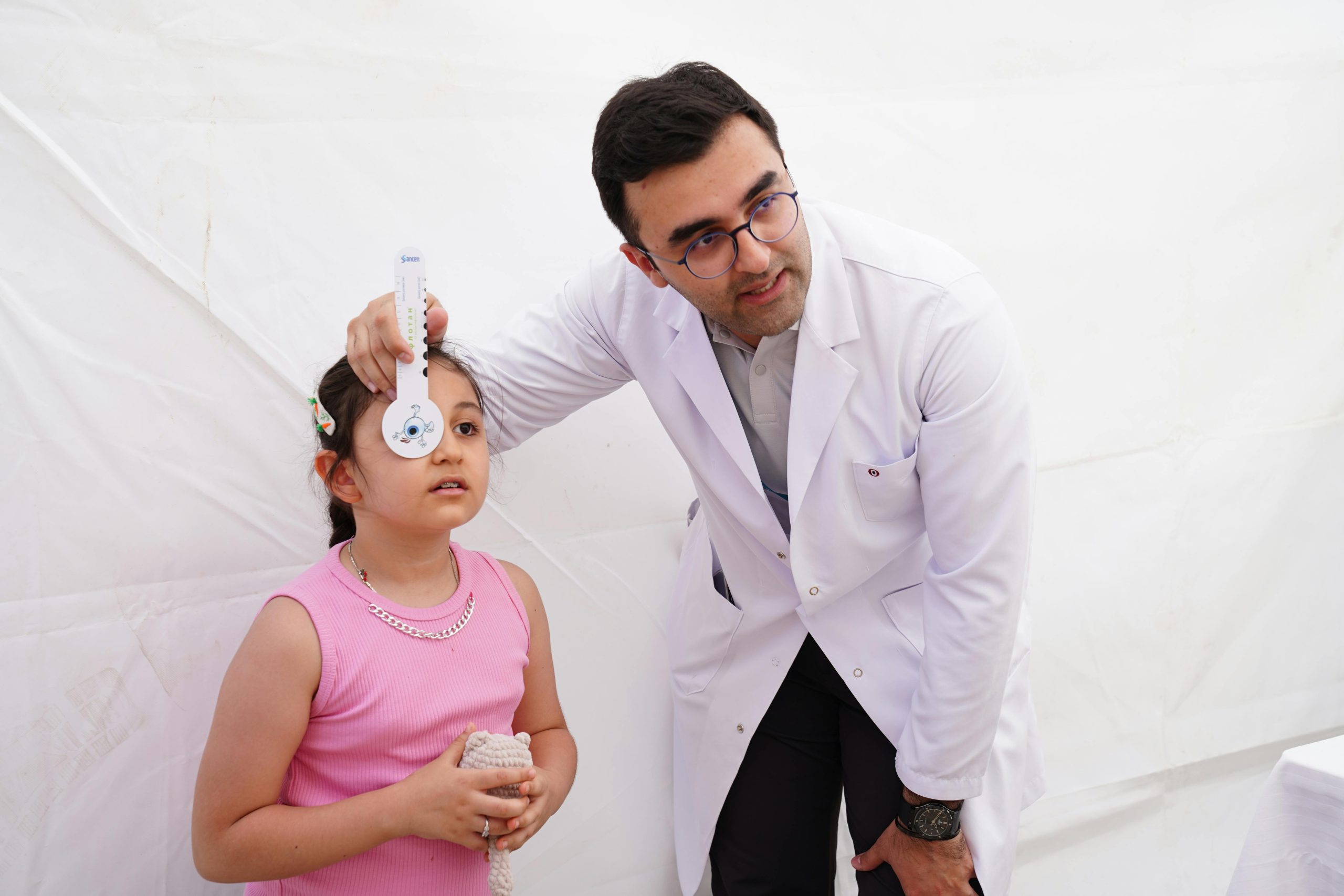 A doctor conducts a vision test on a young girl using an eye chart in a clinical setting.
