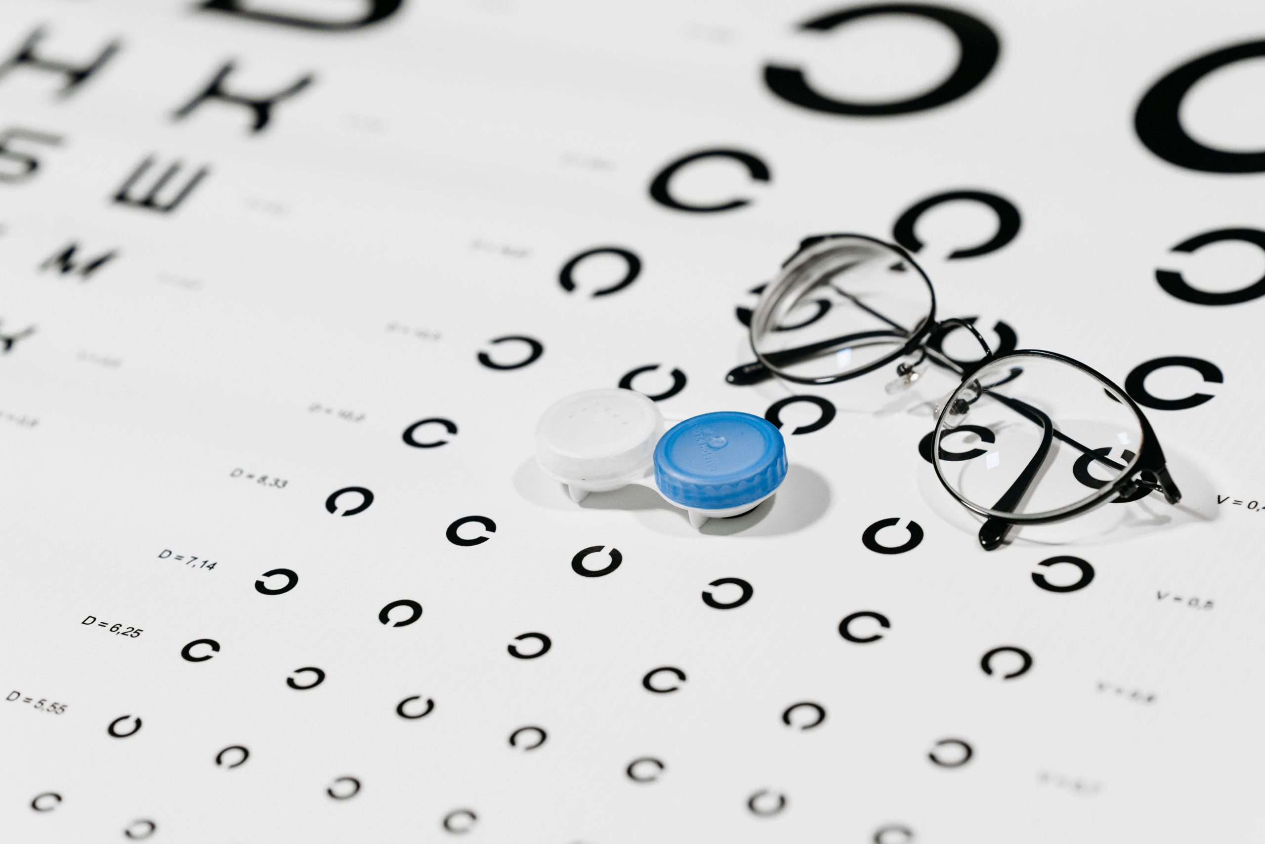 Close-up of contact lens case and eyeglasses on an eye test chart, ideal for vision care concepts.
